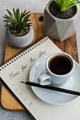 Plans for the day and morning cup of coffee on the table with green plants in the pot