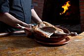Crop faceless male chef standing at table with raw poultry while preparing delicious dish near burning furnace during work in restaurant