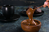 Anonymous crop person mixing dulce de leche in brown bowl against black cup and saucer near chocolate alfajores