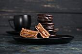 Schokoladen-Alfajores mit Dulce de Leche auf einem Teller in einer Schale neben einer Tasse mit heißer Schokolade