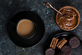 Top view of chocolate alfajores on plate and dulce de leche in bowl placed near cup of hot chocolate