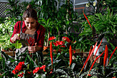 Cheerful young woman in apron spraying clean water on bright tropical flowers and smiling during work in hothouse