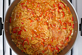 Draufsicht auf gehackte Tomaten und Zwiebeln Valenciana-Reis im Topf, der auf dem Herd für das Mittagessen kocht