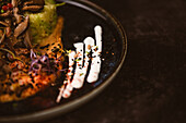 Nahaufnahme eines leckeren veganen Gerichts mit Zucchini-Spaghetti und sautierten Pilzscheiben, bedeckt mit roten Beeren und Alfalfa-Sprossen auf dunklem Hintergrund