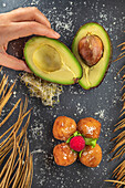From above of crop anonymous cook with ripe avocado halves near appetizing deep fried croquettes with raspberry on top
