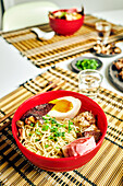 From above of appetizing ramen soup with meat and egg and noodles served in bowl on table near chopsticks and glass cup