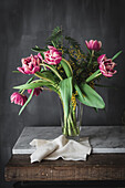 Blossoming pink flowers with gentle petals and green leaves in vase on gray background