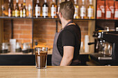 Side view anonymous male barista serving glass of freshly brewed aromatic coffee with ice cubes on counter