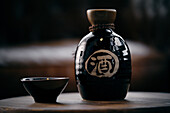 Black ceramic bottle and small bowl with soy sauce placed on wooden table