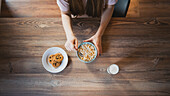 Top view of crop anonymous female with bowl of corn rings between delicious oatmeal cookies and glass of milk indoors