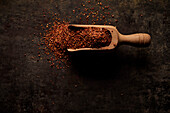 Top view of wooden scoop filled with natural aromatic ground sun dried tomato powder on black background