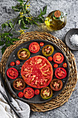 Draufsicht auf köstliche Tomatenscheiben in einem gusseisernen Teller auf einer Korbserviette neben einem Teller mit Meersalz und einem Krug Olivenöl auf einem Betontisch