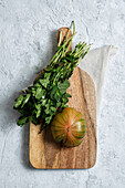 From above of fresh striped green and red tomato placed on wooden cutting board with bunch of mint stems