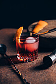 Glass of refreshing alcoholic Negroni cocktail garnished with orange peel and placed on table amidst barman tools