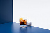 Glas alkoholischer Cocktail mit rotem Wermut, serviert mit Orangenscheiben in einem hellen Studio mit blauer und weißer Wand