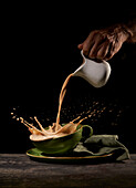 Crop unrecognizable person pouring splashing freshly brewed coffee into green cup on table in kitchen on black background