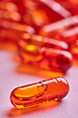 Composition of orange pills scattered on pink background in light studio