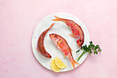 Draufsicht auf rohen Fisch in einem Teller mit Petersilie und Zitronenscheiben auf rosa Hintergrund