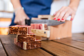 Crop anonymous female seller cutting pieces of eco friendly soap on wooden table in workshop