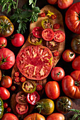 High angle of sliced tomato with salt placed on wooden chopping board among ripe red tomatoes with water drops