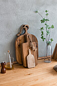 Set of wooden chopping boards in various sizes placed at gray wall on counter with oil in light kitchen at home