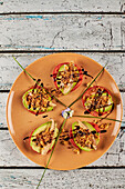 Von oben knusprig gebratene Zwiebel und Makrelenscheiben auf Tomaten- und Avocadoscheiben neben Grünzeug und Blumen auf einem Teller im Restaurant