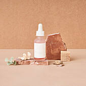 Small bottle of beauty oil and natural handmade soap pieces with pumice stone on two color background
