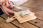 High angle of crop anonymous female cutting with knife bar of handmade soap on wooden chopping board