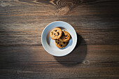 From above of plate with tasty oatmeal biscuits with chocolate chips on wooden table