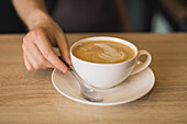 Crop male barista in apron serving cup of coffee while working at bar table in coffee shop