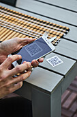 Ernte von oben, nicht erkennbarer Mann, der ein Smartphone benutzt und den QR-Code der Speisekarte eines Restaurants scannt