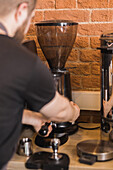 Crop anonymous barista preparing fresh ground coffee in portafilter of professional grinder in cafe