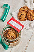 From above homemade chocolate chip Christmas biscuits in glass jars placed on table with ribbons and baubles