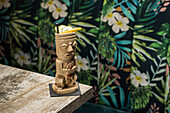 Traditional sculptural tiki cup of alcohol drink with straw placed on wooden table