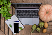 From above of various vegetables arranged on wooden table with gadgets and notepad with pen