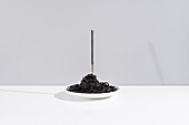 Stainless fork in full bowl of black spaghetti with cuttlefish ink on white table in studio on gray background