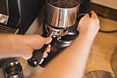 High angle of crop anonymous barista preparing fresh ground coffee in portafilter of professional grinder in cafe