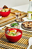 From above of appetizing ramen soup with meat and egg and noodles served in bowl on table near chopsticks and glass cup