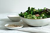 Frischer gesunder Gemüsesalat in einer Schüssel auf einem Tisch mit Olivenöl und Sonnenblumenkernen