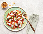 Summery tomato and cod salad in a shallow dish with a fork and a bowl of fried onions