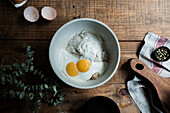 From above bowl with eggs and cream mixed with bread crumbs and flour on wooden table during pastry preparation