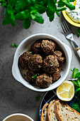 Draufsicht auf appetitliche traditionelle hausgemachte gebratene griechische Fleischbällchen, die auf grauem Hintergrund neben einem Teller mit Brot und Zitrone in der Küche serviert werden