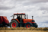 Getrocknete Heurolle und moderner Traktor auf landwirtschaftlichem Feld in bergigem Gebiet im Sommer