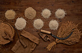 Top view of arranged small heaps of organic grains with fresh beans on wooden table near sickle and bunch of wheat