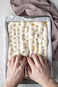 Top view of faceless person preparing raw dough for bread placed on baking paper on table