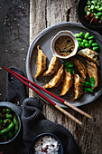 Gyozas with green beans and soy sauce with sesame seeds placed with chopsticks near bowls with spices and pea pods