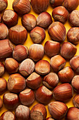 Top view of many whole hazelnuts in shells scattered on bright yellow background