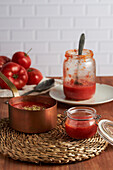 Pfanne und Behälter mit köstlicher hausgemachter Tomatensauce auf einer gewebten Matte auf einem Holztisch in der Küche