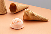 Pink ice cream scoop and waffle cones placed on table in studio