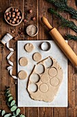 Top view of fresh raw pastry and round shaped cookie cutter placed on table with hazelnuts and Christmas decorations